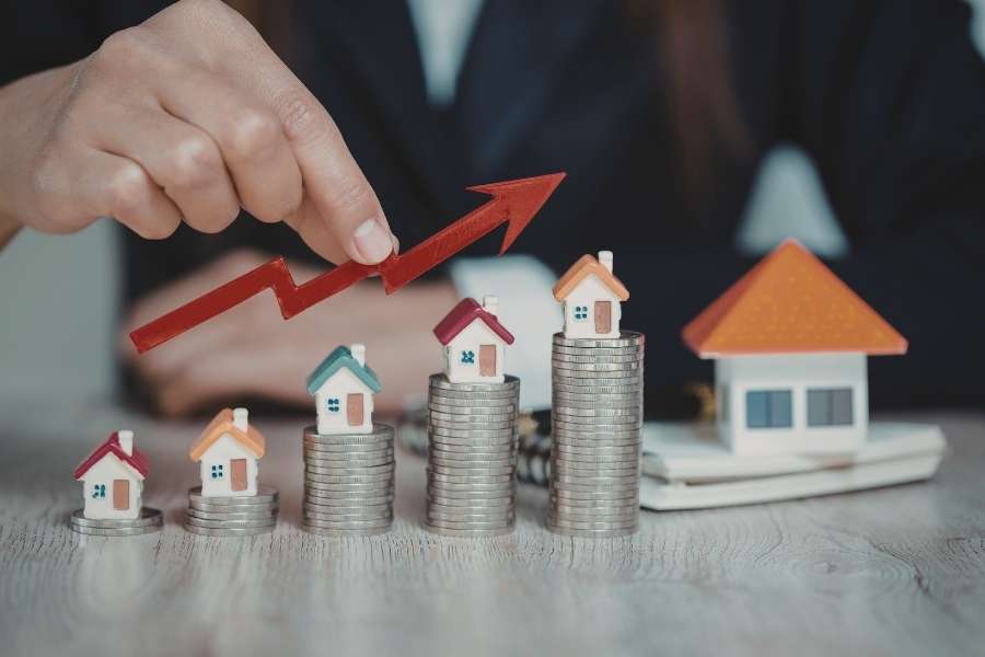 Une main guide une flèche ascendante sur des piles de pièces surmontées de petites maisons, symbolisant la croissance d'un investissement immobilier.