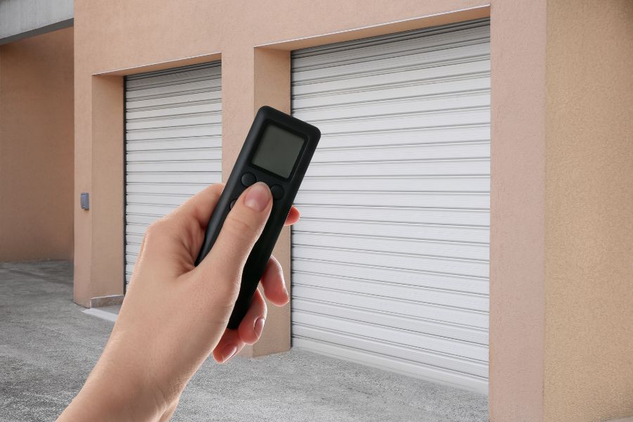 Une main tient une télécommande à écran pour un système de verrouillage à distance pour volets ou portes.